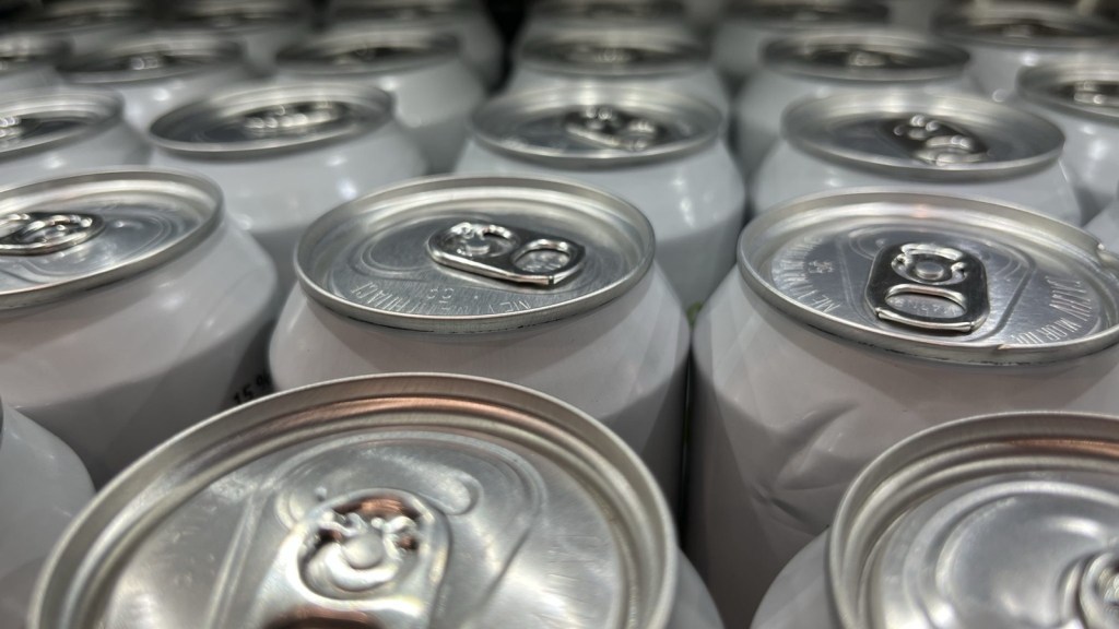 Rows of plain silver drink cans seen from above, their ring-pull tops catching the light