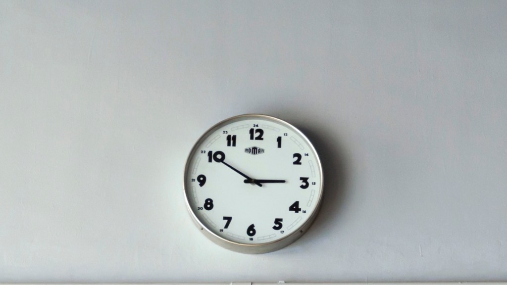 A plain round wall clock with bold black numbers on a pale grey wall, its hands showing about ten to three