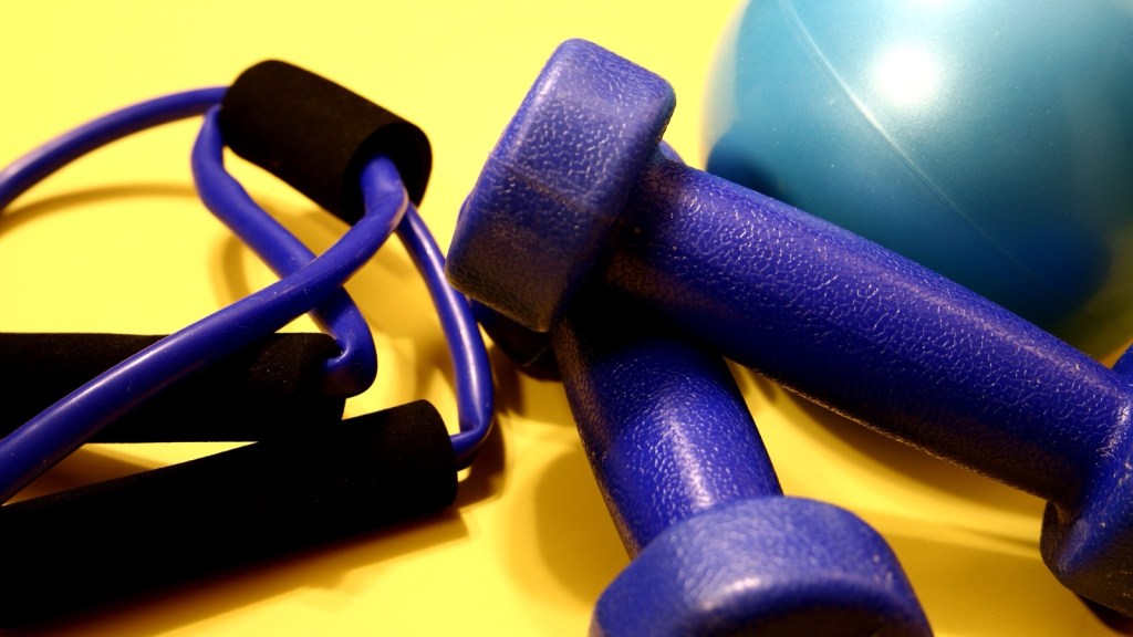 A pair of light blue hand weights, a resistance band with black foam handles and a small teal exercise ball lying on a bright yellow surface