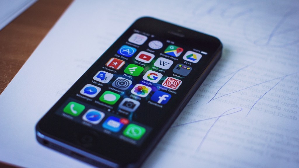 A smartphone lying on a desk on top of handwritten notes, its home screen full of app icons including Facebook, YouTube, Messenger and WhatsApp
